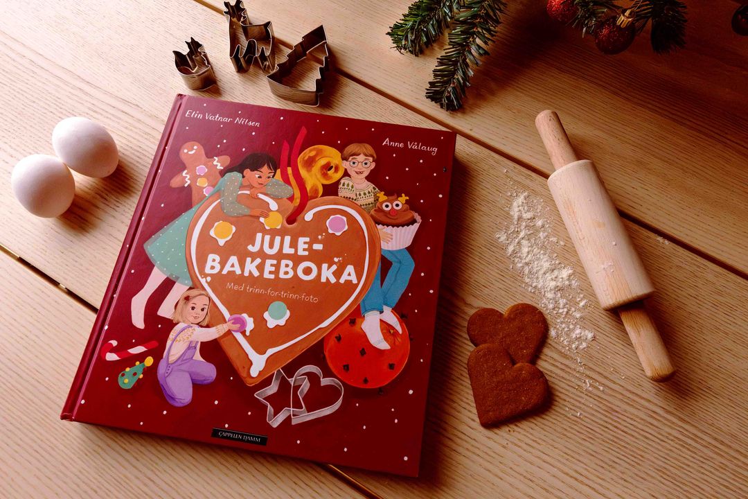Omslaget på barneboken Julebakeboka - 2026 av Elin Vatnar Nilsen. Forsiden viser en fargerik og koselig illustrasjon av barn som baker julebakst på kjøkkenet, utgitt av Cappelen Damm.